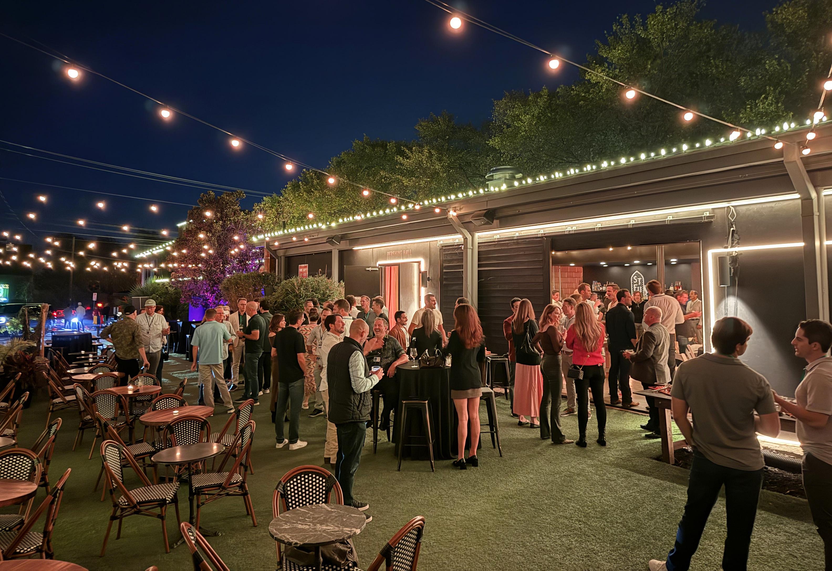 Pershing venue — outdoor patio with string lights, picnic tables, and a crowd of people gathered at dusk in East Austin